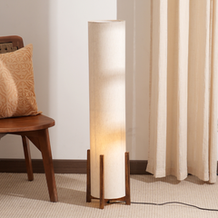 Four Finger Floor Lamp with wooden base and beige shade next to a wooden chair and curtains.