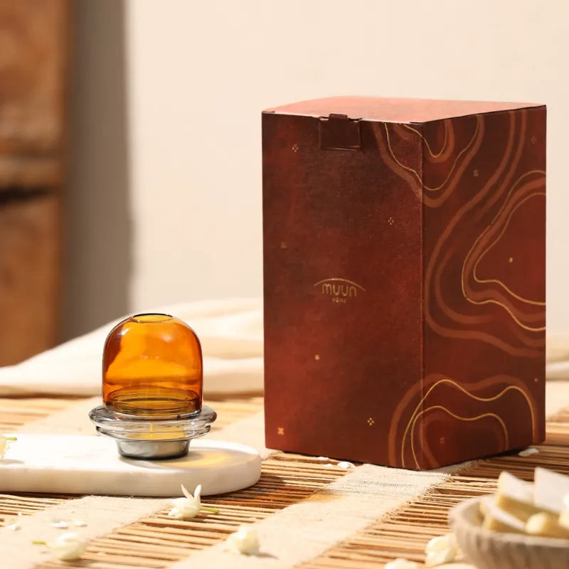Muun Dome Tealight Holder in amber, borosilicate glass dome on slate grey base beside brown gift box