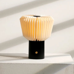 Modern portable table lamp with a black base and pleated shade giving warm ambient light