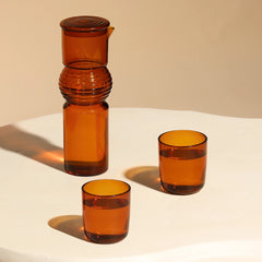 Set of amber glassware including a carafe and two glasses on a white surface with a beige background.