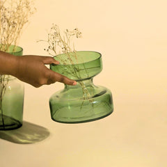 Sage Green tinted glass vase being held by a hand against a beige background