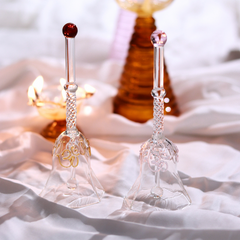 Two decorative glass bells on a soft white fabric background with a blurred candle and bottle in the background.
