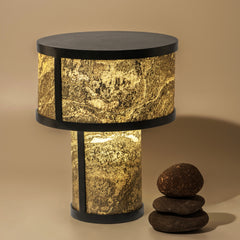 A table lamp with a thin layered natural stone sheet and a hand-fabricated mild steel base, illuminated, alongside two rocks for scale.