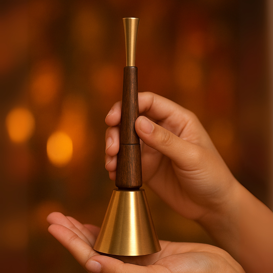 Hand holding a wooden and brass bell against a warm, blurred background