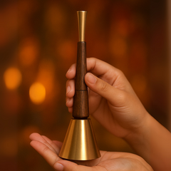 Hand holding a wooden and brass bell against a warm, blurred background
