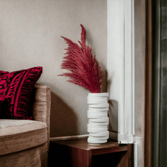 A minimalistic decorative Yugen vase with stack pieces design in white and a red floral-like decoration on top placed on a side table