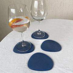 A set of four blue frosted glass coasters placed on a table with two glasses of water and a muddler.