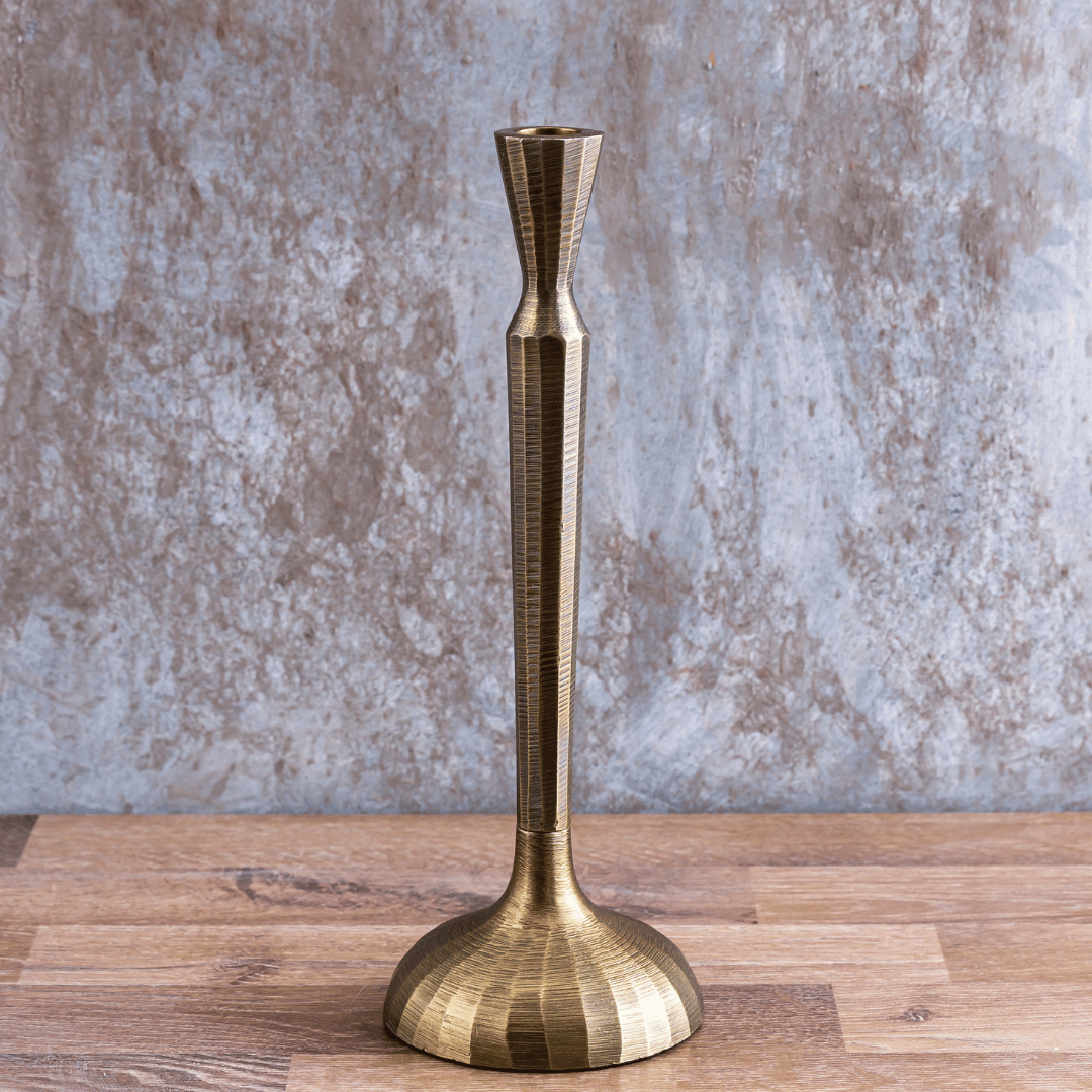 An antique brass finish Tvisa Candle Holder placed on a wooden surface against a textured background.