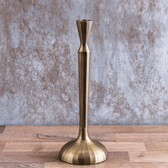 An antique brass finish Tvisa Candle Holder placed on a wooden surface against a textured background.