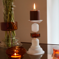Kanak candle in a decorative holder in Borosilicate white and amber glass on a reflective surface with a blurred background