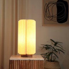 A lit Serenity Table Lamp with a natural European linen shade and a mango wood base, placed on a wooden stool