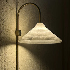 Close view of Conical Wall-mounted lamp with a textured white shade and gold fixture casting a warm glow on a textured wall.