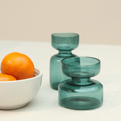 Two borosilicate glass mini vases gift set in teal, placed on a table with a bowl of oranges in the background.