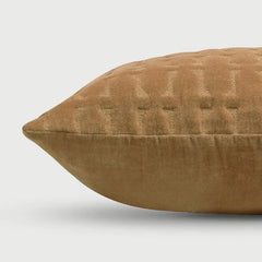 A close-up of a textured, quilted throw pillow in a warm camel brown color, showing its fabric weave and stitched details against a light gray background.
