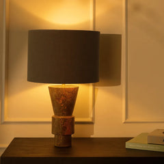 Decorative Ameo Table Lamp with a dark fabric shade & marble base on a wooden surface, illuminated by warm light.
