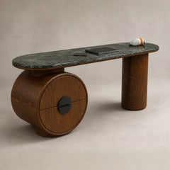 A modern sculptural console table featuring a dark green marble top and a round wooden base with a cylindrical leg, shown against a neutral beige background.