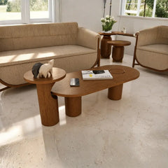 A modern living room scene featuring a low, organic-shaped wooden coffee table with chunky cylindrical legs, accompanied by matching wooden side tables and a beige upholstered sofa.