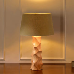 Foresta Table Lamp with textured wooden base and fabric shade with warm glowing light on a reflective surface.