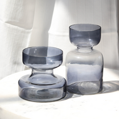 Two smoked slate grey glass vases on a white surface with a white curtain background