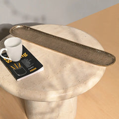 Long narrow textured dosa tray on a round marble table surface with a white mug and book.