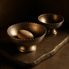 Two arc bowls made of aluminum on a dark surface with a single stone inside one of them.