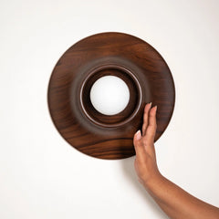 Round Paten Wall Light made of teakwood with a hand reaching towards it on a white background