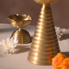 close look of brass diyas, one tall and one short. The diyas have a metallic bronze finish and are handcrafted. 