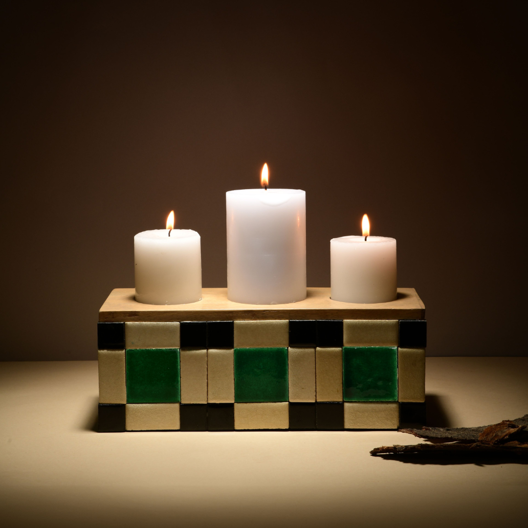 Three white candles on a decorative Blade of Grass Candle Holder made of wooden block with a checkered pattern against a dark background. 