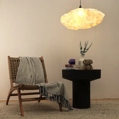 Wicker chair with a patterned throw blanket, small table with decorative cloud shared pendant light in a room.