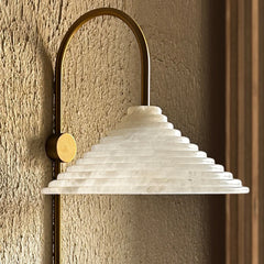 Decorative Wall-mounted light with a textured white shade and brass arch on a textured wall.