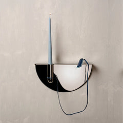 Designer semi-circular wall-mounted candle holder with a black and white mirrored finish, holding a light blue taper candle, shown against a textured light gray wall.