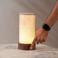 A cylindrical magnus table lamp with a beige shade and a wooden base, illuminated light.
