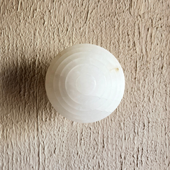 Skive Wall Sconce, close view of white spherical alabaster stone globe on a beige textured wall