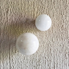 Two smooth white polished alabaster stone sphere wall sconces resting on a textured beige surface.
