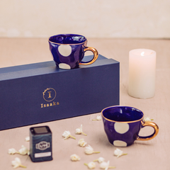 Two blue cups with gold detailing, a tea tin, and a candle, all presented with the branding gift box