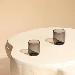 Two smoked glass tumblers on a white pedestal 