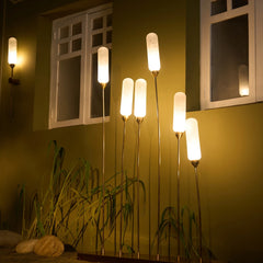 Decorative Kinara outdoor floor lamps with cylindrical lights placed next to garden wall.