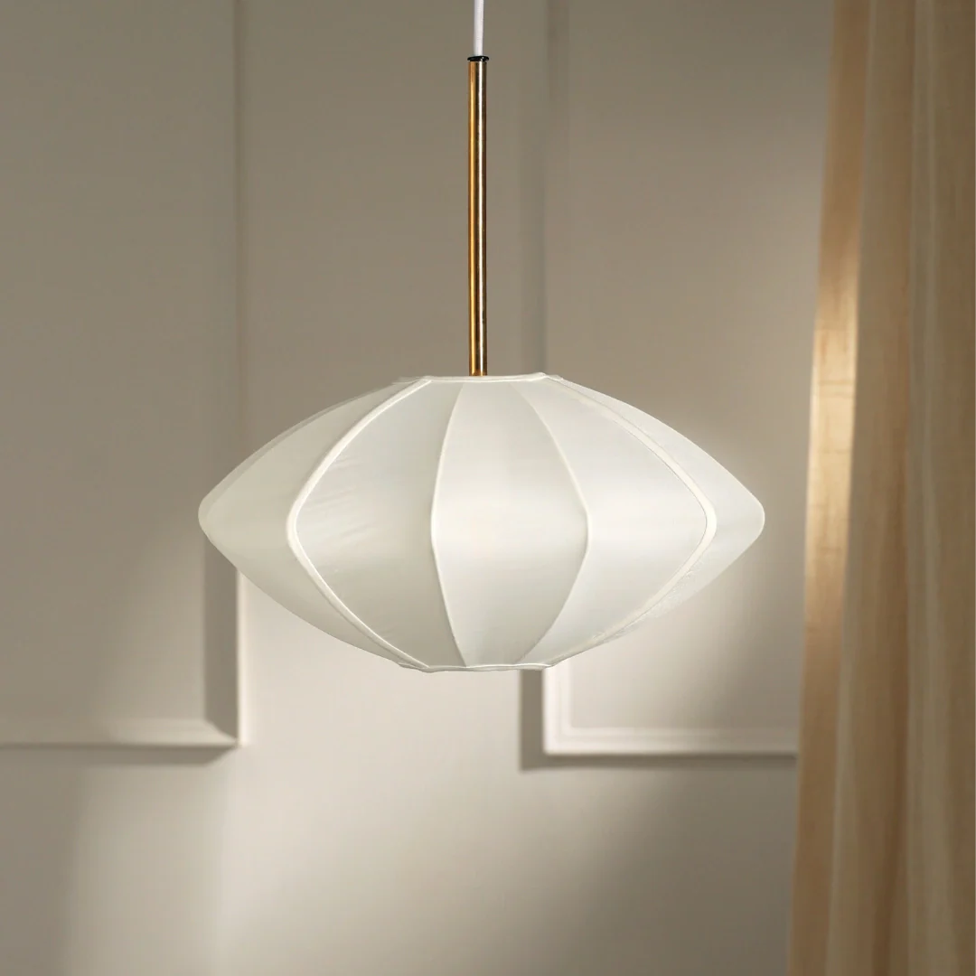 A modern pendant lamp with a white and gold geometric design shade, suspended by a brass-like rod, against a neutral background.