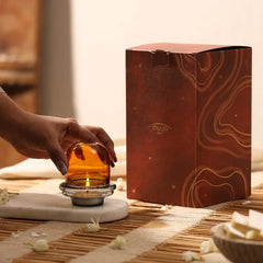 Muun Dome Tealight Holder in amber, hand placing glass dome over lit tealight, gift box in background