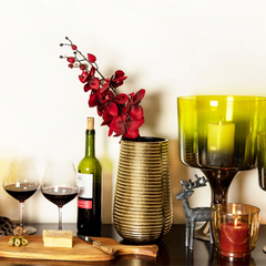 Decorative Bhrama Vase made of aluminum in gold finish with textured lines placed on a table with red flowers