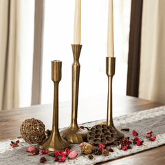 Three tall antique brass finish Tvisa candle holders with textured surface placed on a wooden table