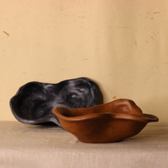 Two ceramic bowls, one black and one brown, on a beige surface with a beige background.