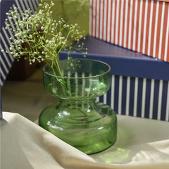 A green glass vase placed next to blue and red decorative gift boxes with striped patterns