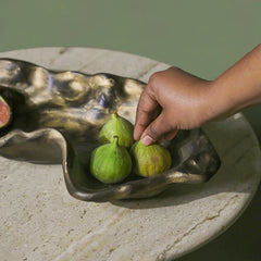 Hand picking a fig from a decorative metal bowl on a stone surface.