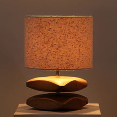 Decorative Sabbia Table Lamp with a textured white shade and wooden base on a reflective surface.