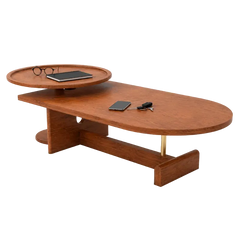 A modern oval coffee table in a warm medium-brown wood finish, featuring a built-in circular tray on top, a small gold metal support leg, and a few small lifestyle props (glasses, tablet, phone, keys) placed on its surface, set against a solid white background.