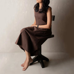 A woman seated on a black stool wearing a sleeveless brown midi dress.