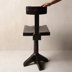 A dark wood swivel barstool with a unique wavy seat and backrest, shown with a hand holding.
