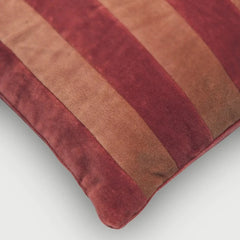A close-up of a Holly Spice Velvet Stripe Cushion Cover in shades of deep red, terracotta, and warm brown, showing the soft texture of the fabric.