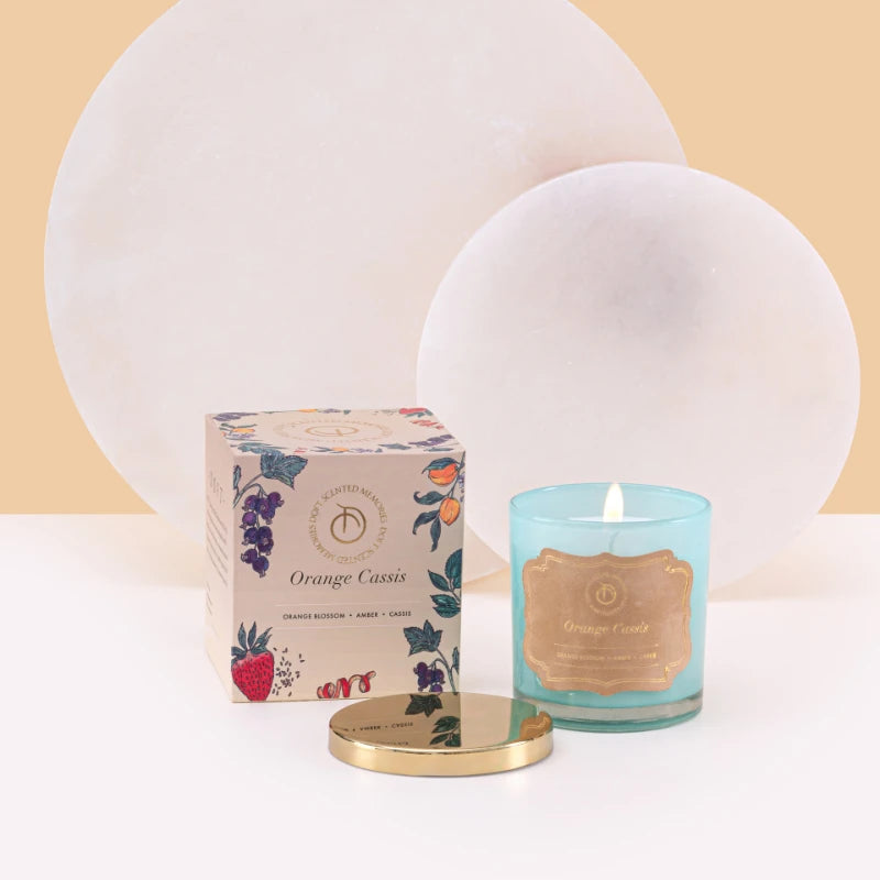 Illume Midi - Lid Jar Candle - Aqua - Orange Cassis - Set of 2, lit aqua glass jar with gold lid beside Orange Cassis box